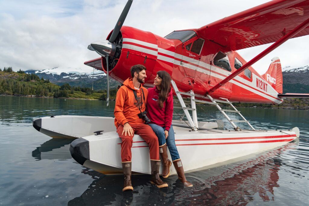 Couple sits on the float of Rust's Flying service red De Havilland Beaver