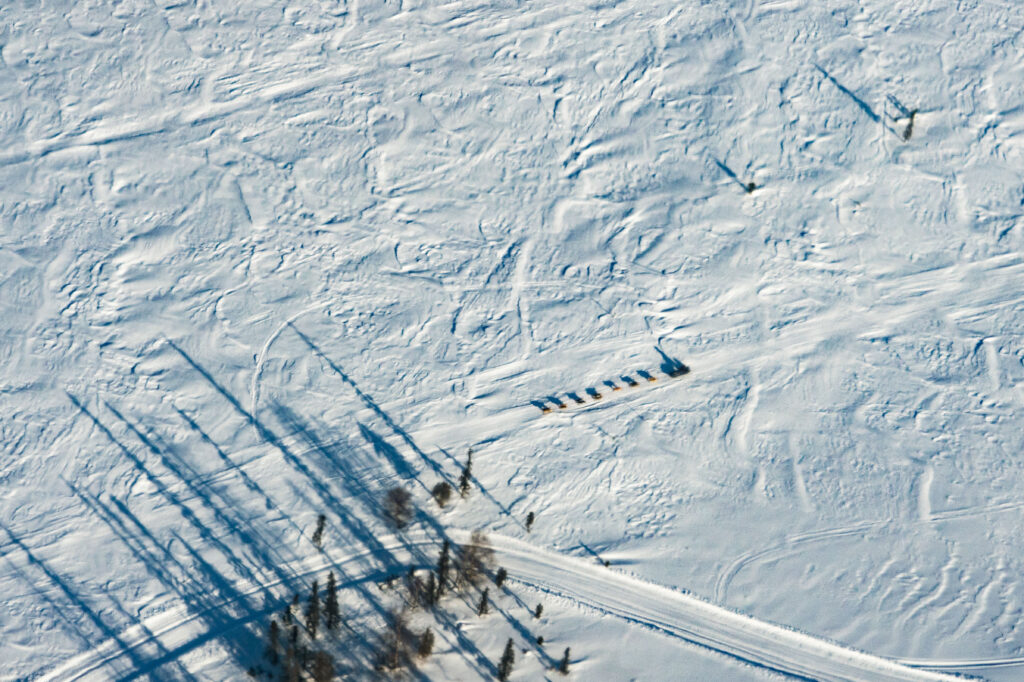 Mushers and dogs with sled seen aerially running the Iditarod trail